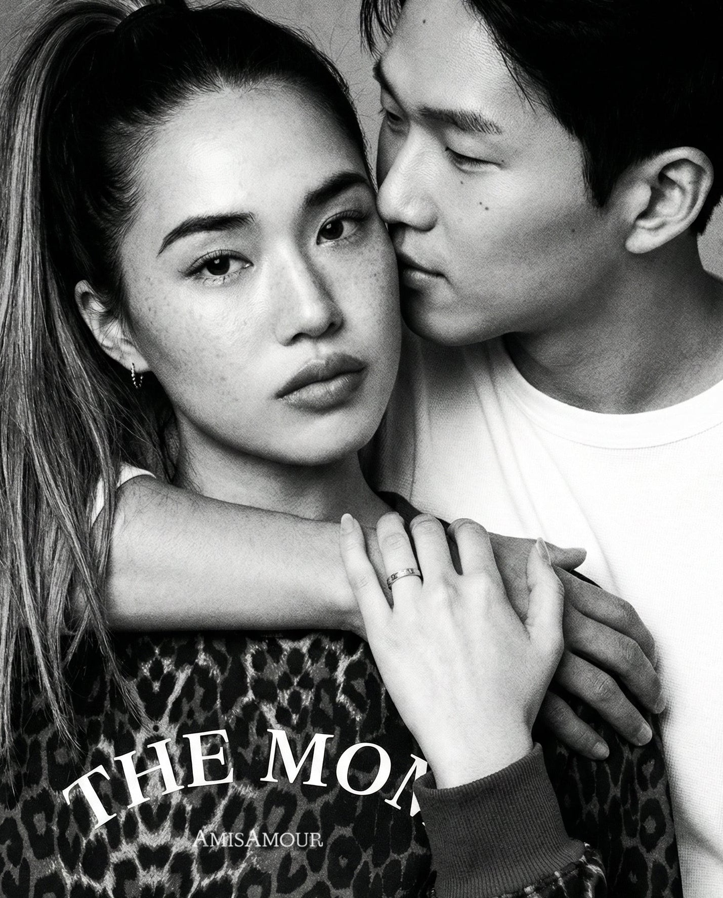 Black and white photo of a couple embracing, with one person wearing a leopard print AmisAmour sweater with THE MOM text.